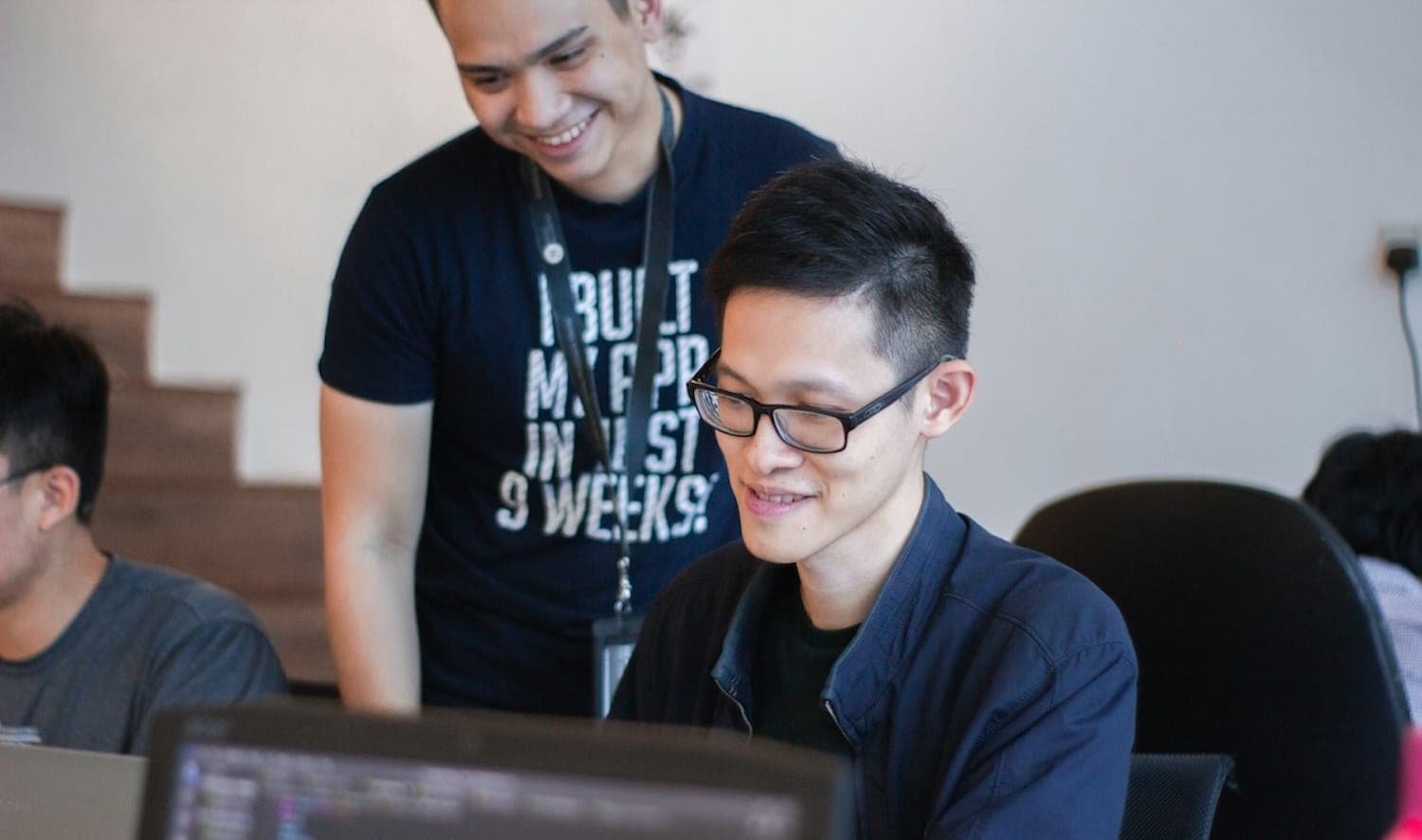 Image shows two people looking around a computer. 