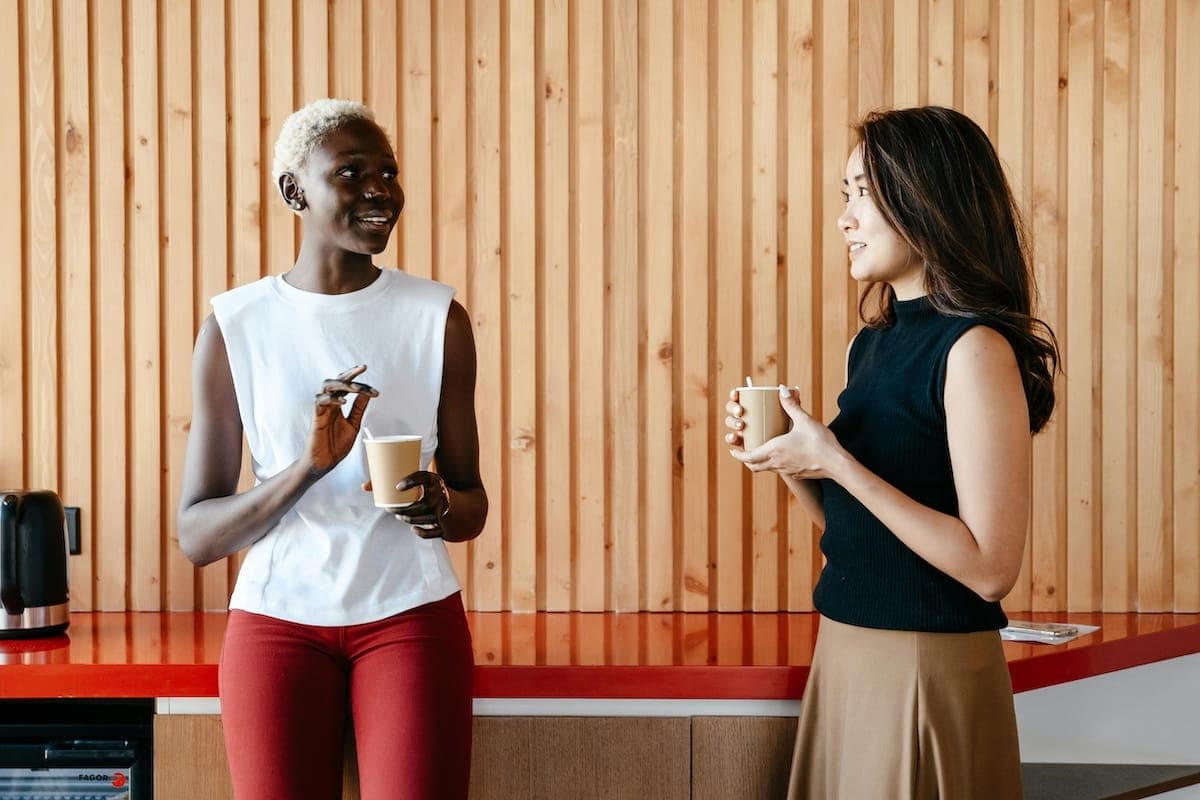 Two women talking in office staff room and making tea