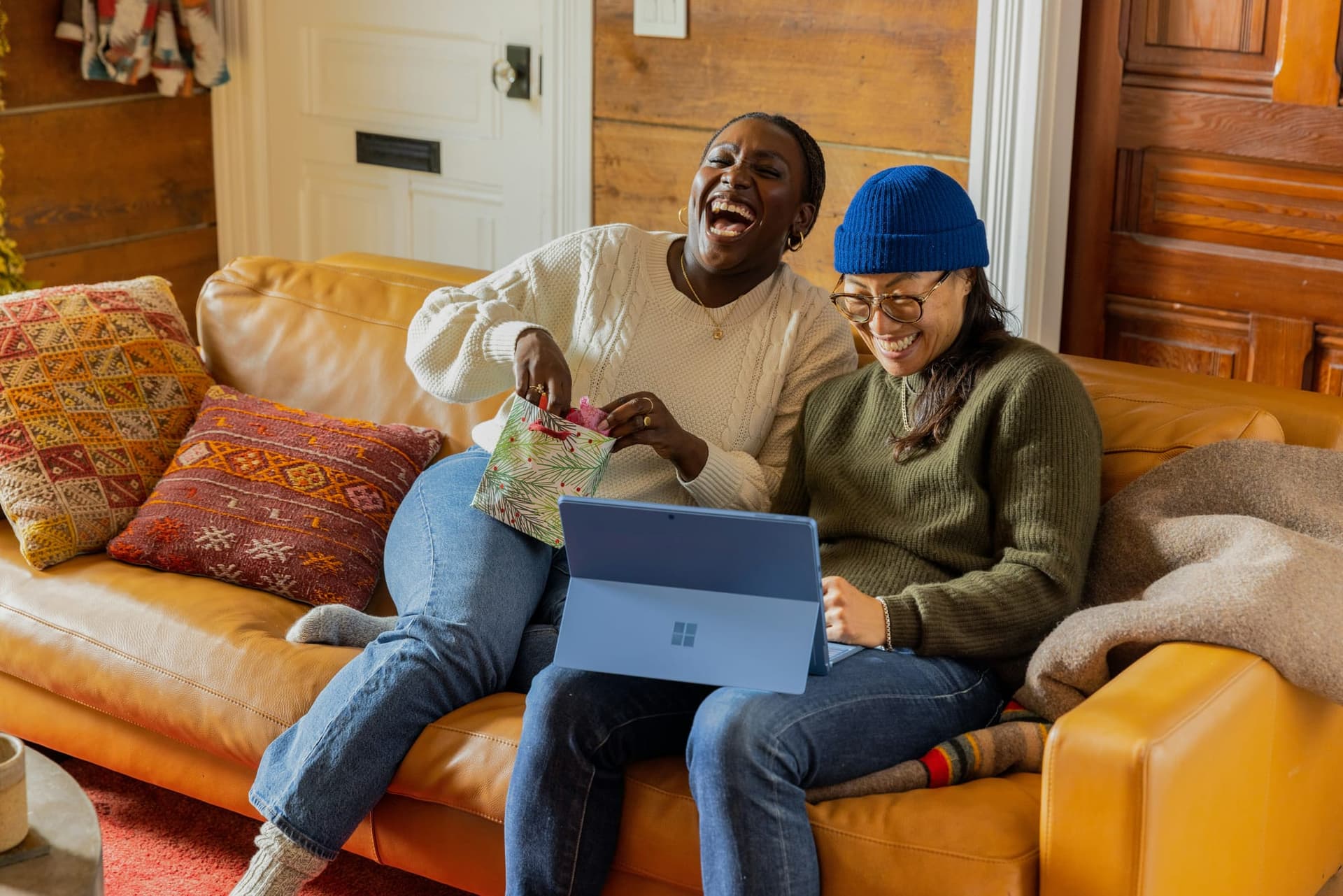 Image shows two people laughing together over a laptop sat on a sofa. 