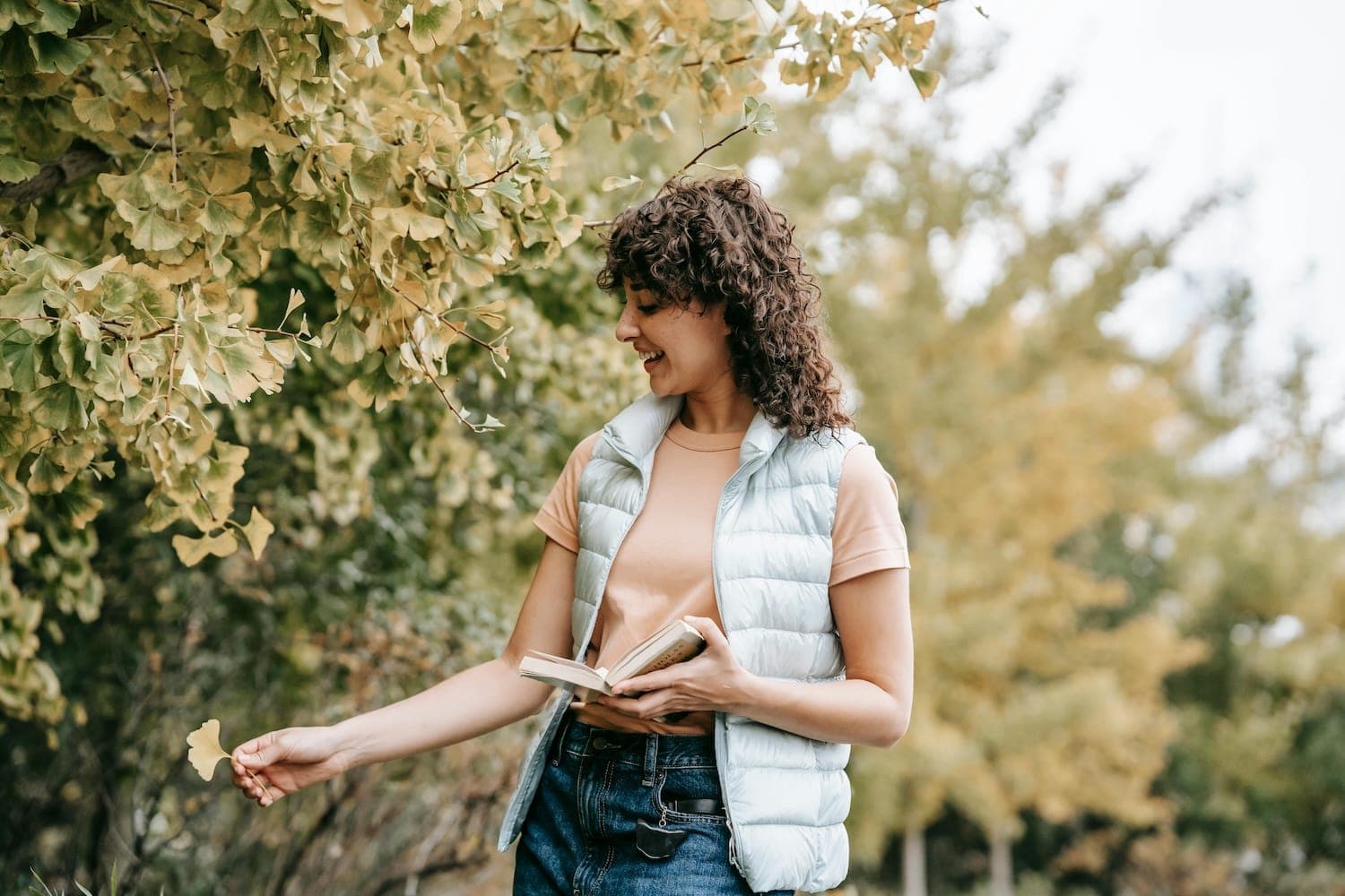 Woman walking in nature with book in hand noticing foliage