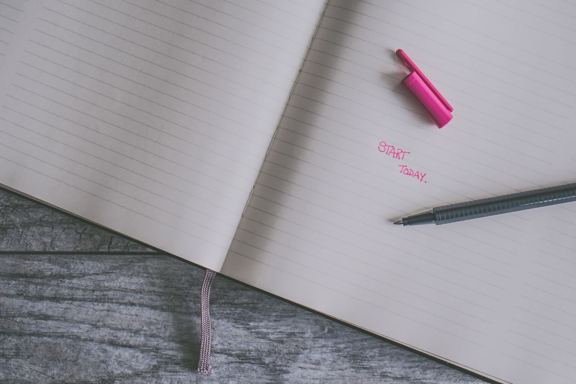 Close-up of an opened lined notebook, a pen laying on the pages with the words 'start today' written
