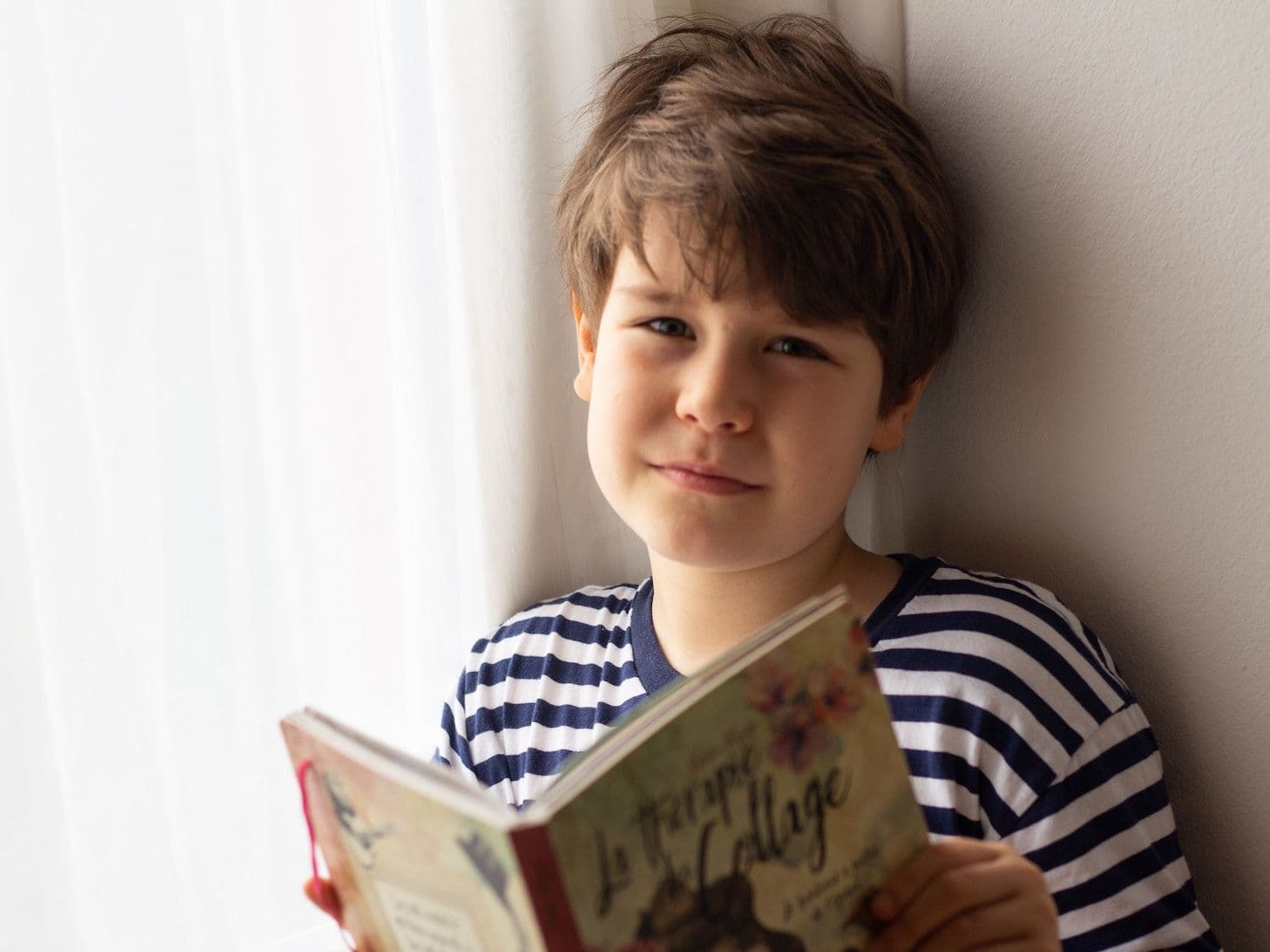 Boy looking at the camera holding an open book.