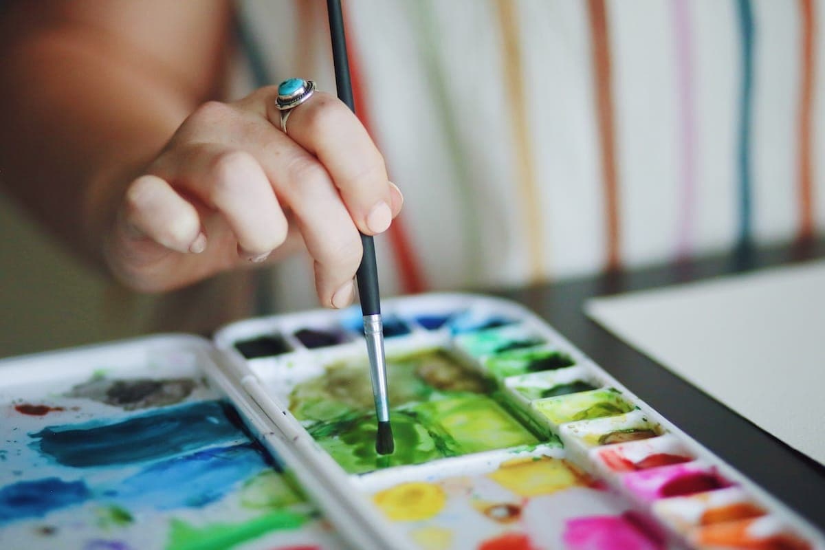 Person dipping paint brush into green paint.