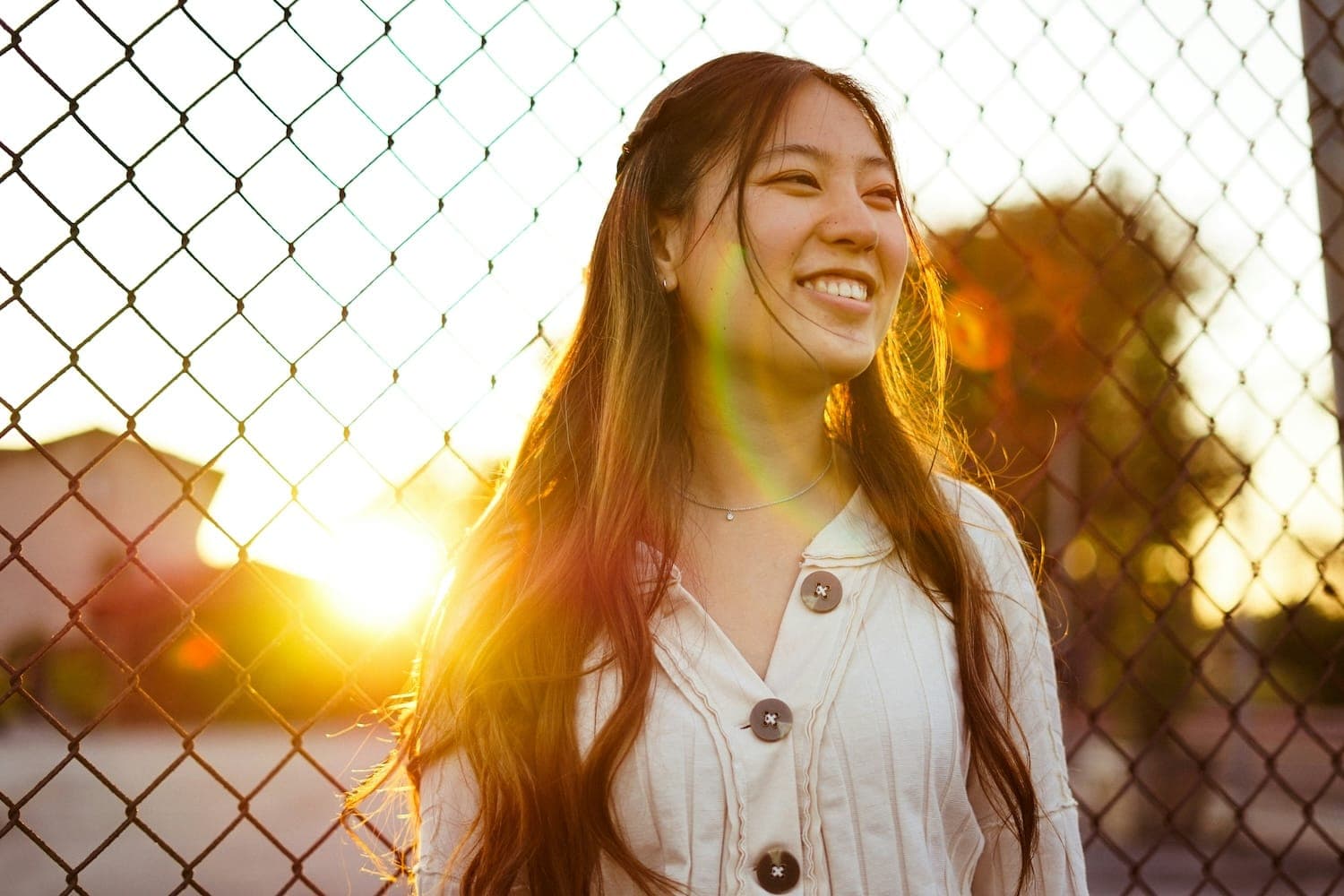 Image shows a girl smiling with the sun setting behind her.