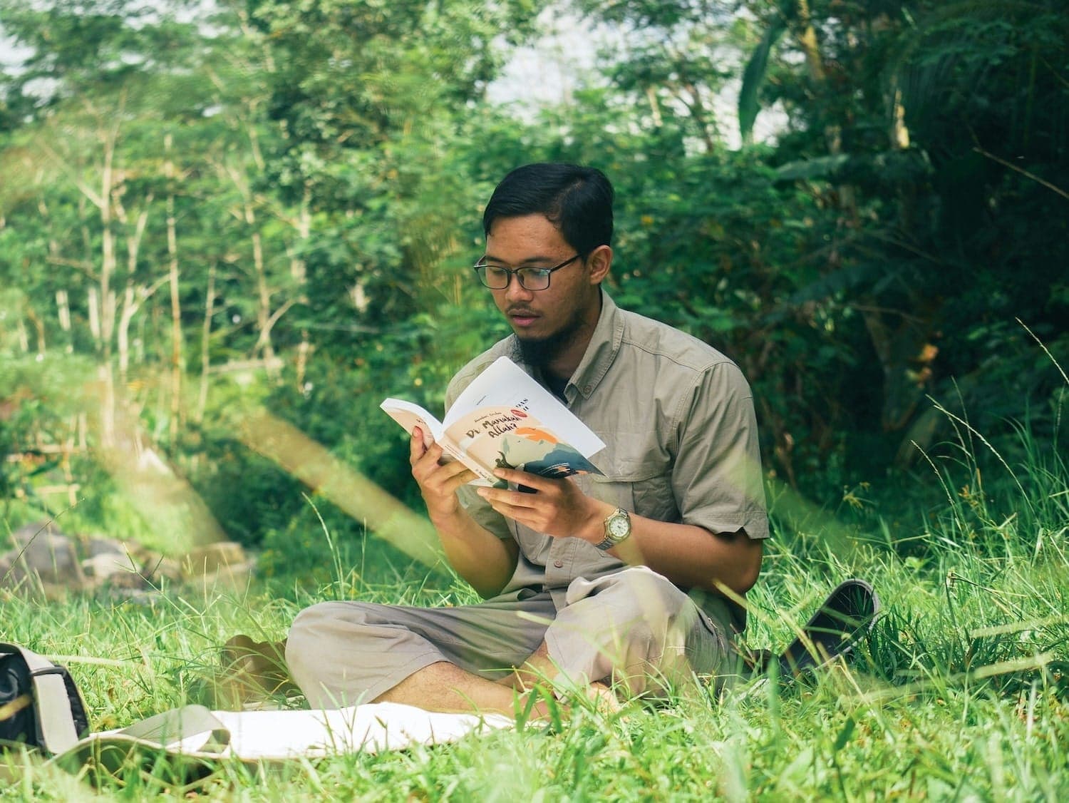 Image shows man reading a book in a field.