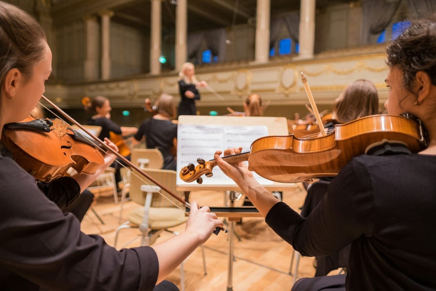 Image shows people playing the violin in an orchestra.