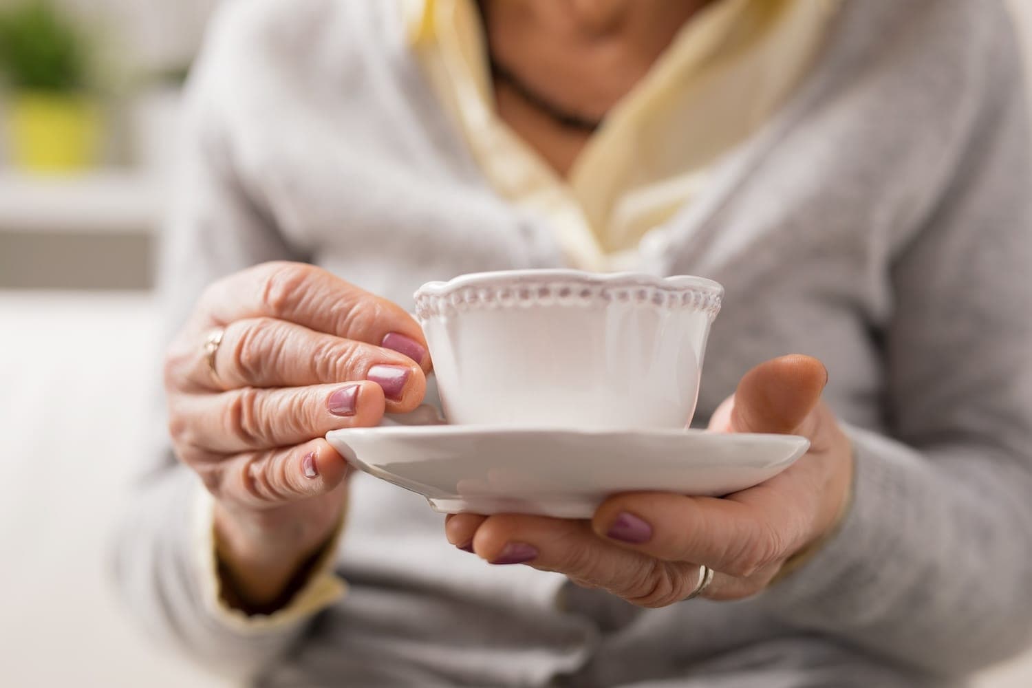 Image shows older person holding a cup and saucer.